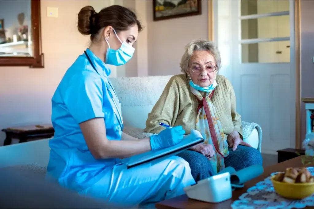 A smiling elderly woman sitting comfortably in her living room with a caregiver by her side